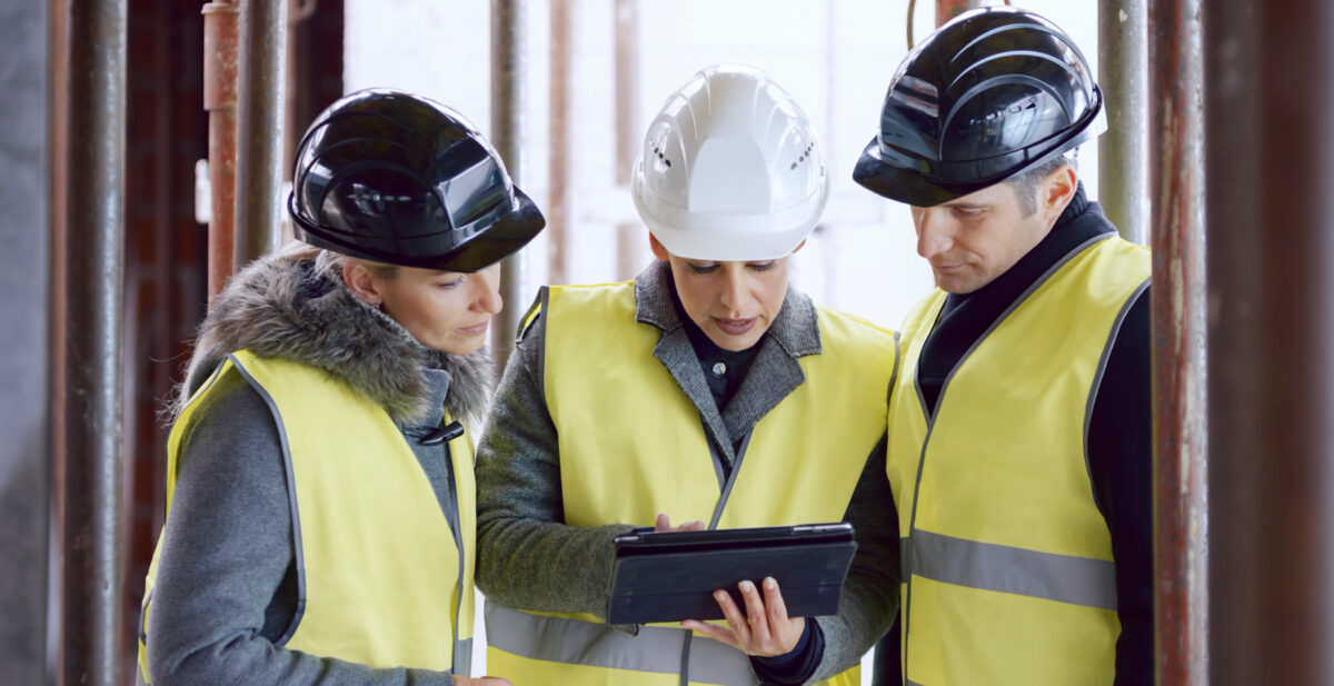 Femme architecte tenant une tablette numérique et expliquant les détails d'un plan de construction à des investisseurs masculins et féminins.